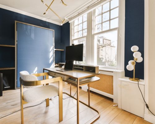 a home office with blue walls and white trim on the walls, wooden floors and a desk in front of a large window