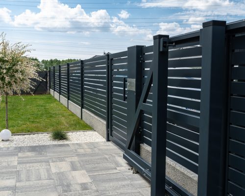 A modern panel fence in anthracite color, a visible sliding gate to the garage and a wicket with a letterbox.