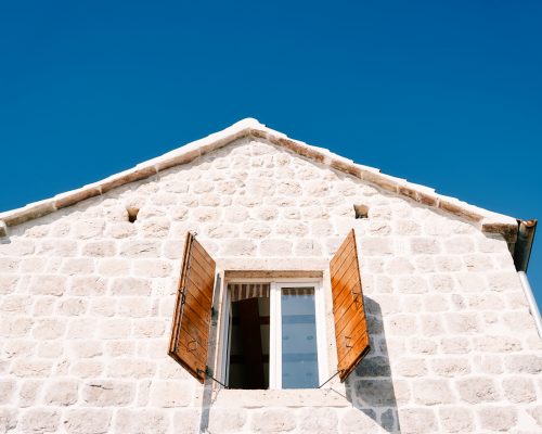 Open wide wooden shutters of the attic window of an ancient stone house. High quality photo