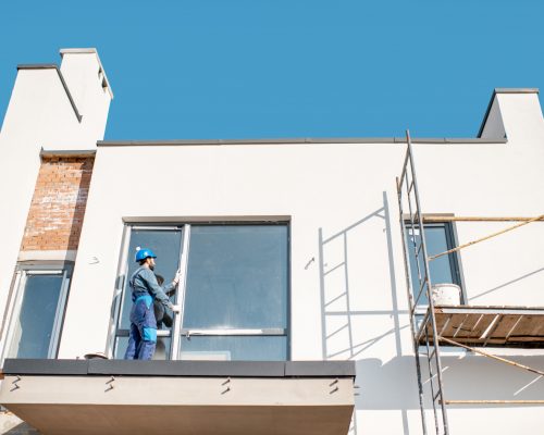 White building facade with workman in uniform mounting the window on the balcony